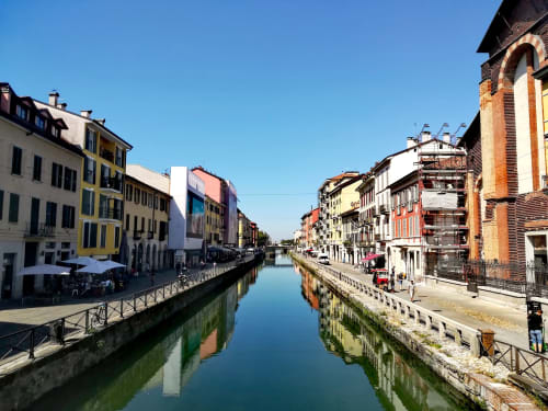 Canale Navigli a Milano con edifici colorati, riflessi d'acqua blu e passerella sul lungomare vicino a Porta Tosa