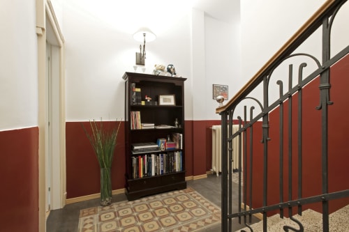 Corridoio Porta Tosa Milano con pareti rosse, libreria scura, ringhiera ornamentale e piastrelle a motivi geometrici