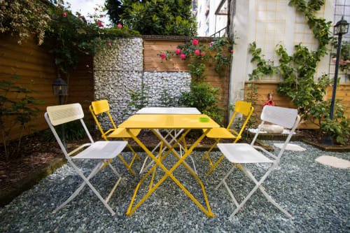 Cortile Porta Tosa Milano con tavolo giallo e sedie bianche circondate da muri decorati e fiori rampicanti