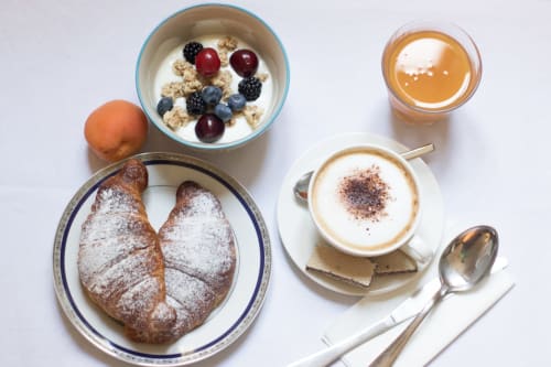 Colazione a Porta Tosa Milano con cornetto, ciotola di cereali ai frutti di bosco, cappuccino e caffè