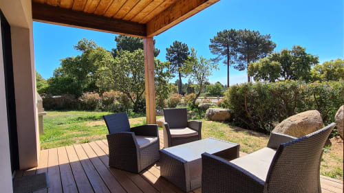 Covered wooden terrace at Villas Lantana with rattan seating, table, and views of Corsican gardens and trees