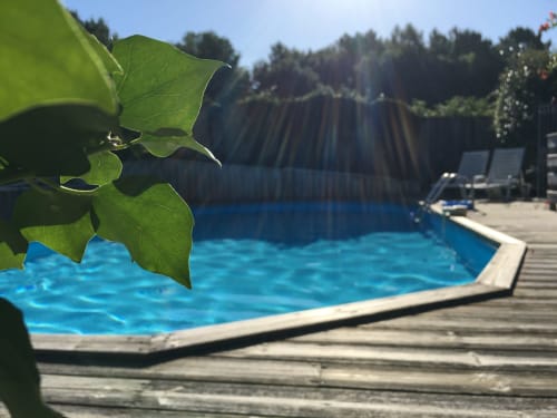 Superbe piscine bleu vif avec terrasse en bois à Sous Les Marronniers, Petit Palais Cornemps, entourée de verdure et de forêt