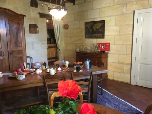 Salle à manger du Sous Les Marronniers avec murs en pierre, mobilier en bois et fleurs d'hibiscus rouges à Petit Palais Cornemps