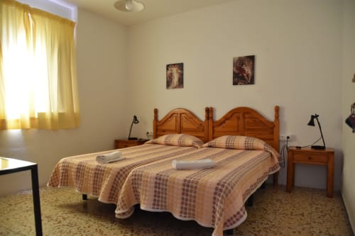 Habitación de la Pensión Eva en Puerto de Mogán con cama de madera, ropa de cama a rayas y cortinas amarillas