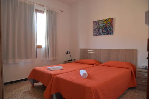 Luminosa habitación de albergue en Pension Eva, Puerto de Mogán, con camas gemelas, ropa de cama naranja, ventana y colorido arte mural