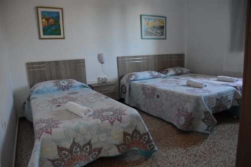 Habitación doble en la pensión Eva de Puerto de Mogán con dos camas, colchas estampadas y decoración mural