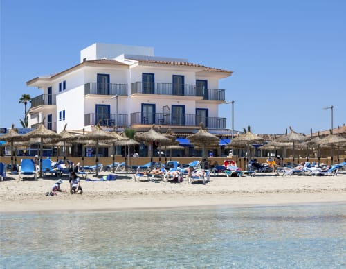 Hotel Sa Roqueta beachfront property in Can Picafort with white building, thatched umbrellas, and sandy beach