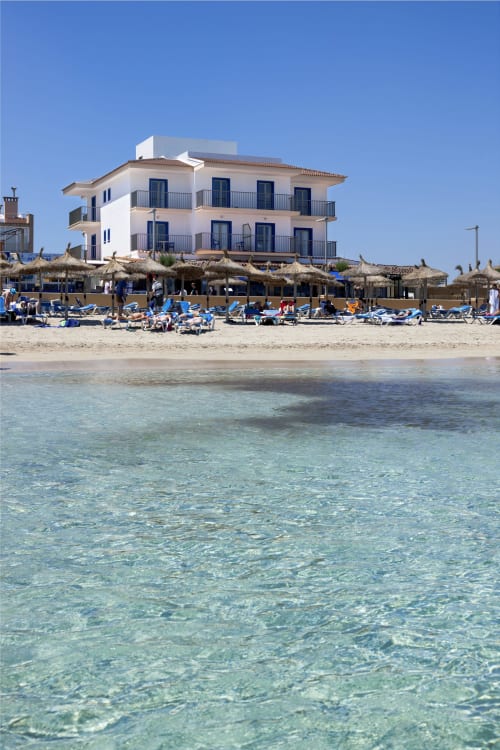 Hotel Sa Roqueta beachfront view with clear turquoise water, blue loungers, and straw umbrellas in Can Picafort