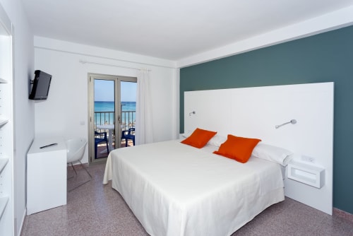Modern hotel bedroom at Hotel Sa Roqueta in Can Picafort with sea view balcony, white bed, and teal accent wall