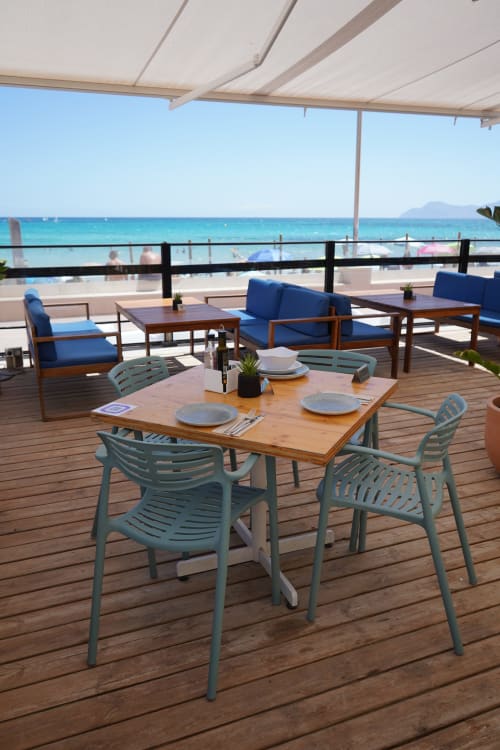 Hotel Sa Roqueta beachfront terrace with dining table, blue chairs, and Mediterranean Sea view in Can Picafort