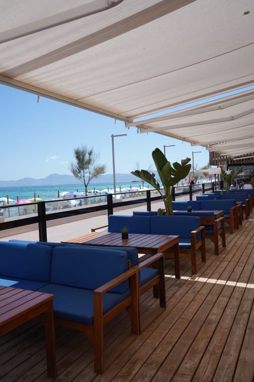 Hotel Sa Roqueta beachfront terrace in Can Picafort with blue seating, wooden deck, and Mediterranean sea views.