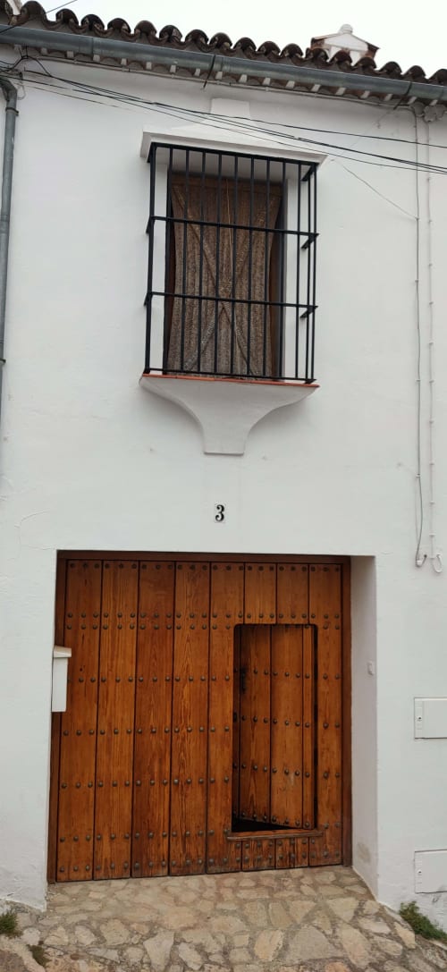 Traditional white-walled entrance to La Casa De La Abuela Regina in Grazalema with wooden door and barred window