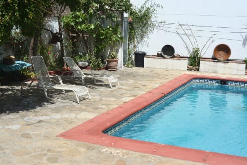 Sunny poolside at La Casa De La Abuela Regina in Grazalema with lounge chairs, terracotta deck, and lush vegetation