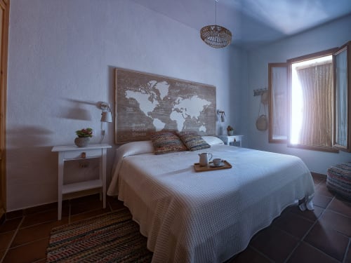 Dormitorio luminoso en Apartamento Simancón, Grazalema con cama blanca, mapa mundial, paredes azules y acceso a balcón