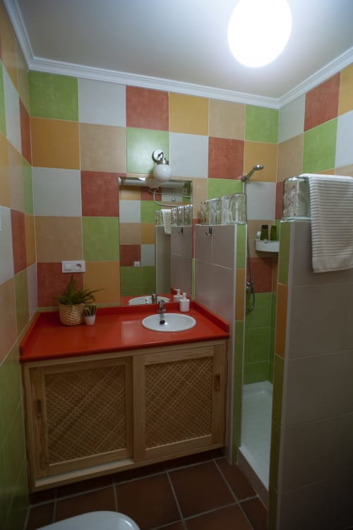 Colorful bathroom at Apartment Pinsapar in Grazalema with red countertop sink, patterned wooden vanity, and tiled shower
