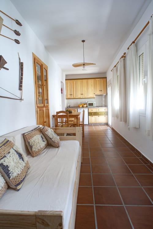 Bright apartment living space with wooden sofa, terracotta tiles, equipped kitchen, and white walls at La Casa De La Abuela
