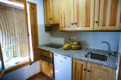 Cocina compacta con muebles de madera, encimera de granito, azulejos azules y ventana en apartamento de Grazalema
