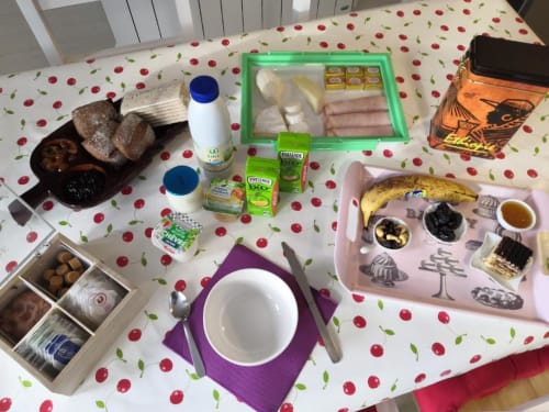 Petit-déjeuner garni au Sci Saviya B&B d'Égletons avec pain, jambon, produits laitiers, viennoiseries et confitures sur motif cerises