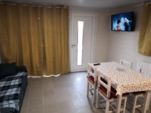 Studio cosy du Sci Saviya BnB à Égletons avec table à manger, canapé, TV et rideaux jaunes