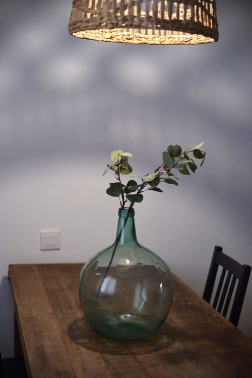 Rama de eucalipto en florero de vidrio verde sobre mesa de madera bajo lámpara colgante de ratán en La Casa De La Abuela Regina, Grazalema