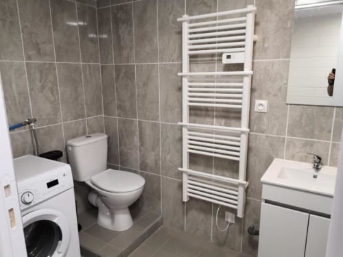 Salle de bain moderne de l'appartement Sci Saviya à Égletons avec toilettes, lavabo, porte-serviettes blanc et machine à laver