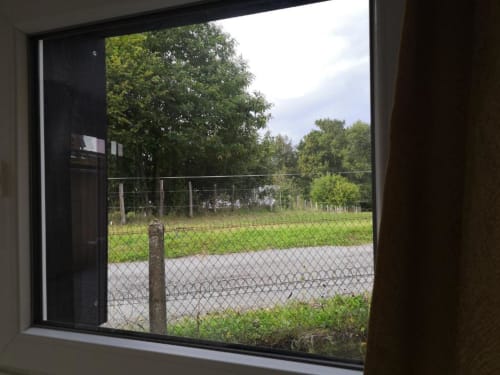 Vue du jardin depuis la fenêtre de l'appartement Sci Saviya à Égletons, avec pelouse clôturée et arbres