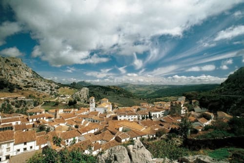 Aerial view of Grazalema village with white-walled houses, terracotta roofs, and surrounding mountains under blue sky