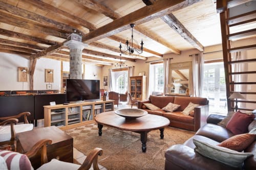 Rustic cottage living room at Les Lumières du Causse with exposed wooden beams, brown leather sofa, TV, and mountain views in