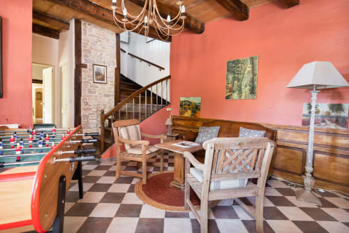Rustic cottage living area with coral walls, foosball table, wooden furniture and spiral staircase at Les Lumieres Du Causse
