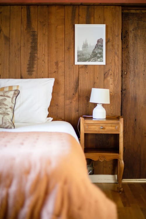 Rustic wooden bedroom at Les Lumieres Du Causse with mountain view framed art, white bedding, and wooden nightstand with lamp