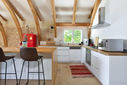 Cuisine loft moderne aux poutres en bois, meubles blancs, cafetière rouge et bar des Lumieres Du Causse