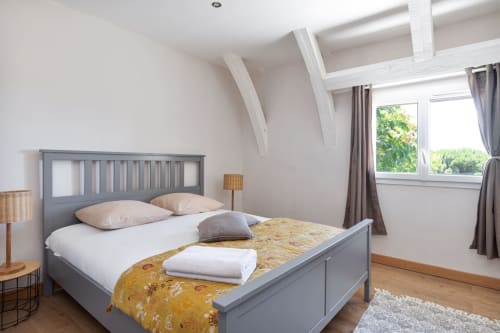 Chambre lumineuse sous les toits aux Lumieres Du Causse avec lit gris, poutres blanches, vue sur jardin et parquet