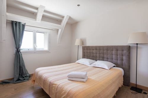 Chambre lumineuse aux Lumières du Causse avec lit queen, tête de lit grise, puits de lumière et parquet