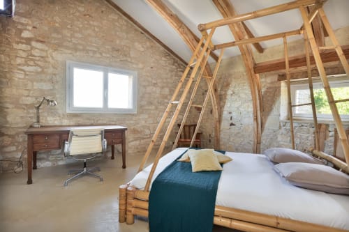 Chambre mansardée La Grange Haute avec lit à baldaquin bois, murs en pierre, coin bureau et poutres apparentes aux Lumières Du Causse