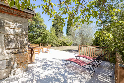 Terrasse ensoleillée des Lumieres Du Causse avec chaises longues, mobilier en bois et vue sur un jardin luxuriant à Bellefont