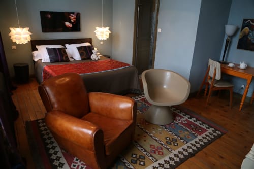 Modern bedroom at Le Grand Duc in Valenciennes featuring cognac leather chair, pendant lights, and red bedding with city view