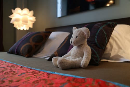 Ours en peluche sur le lit de la chambre Rêves d'Enfance au Le Grand Duc B&B, Valenciennes, avec coussins décoratifsand éclairage ambiant