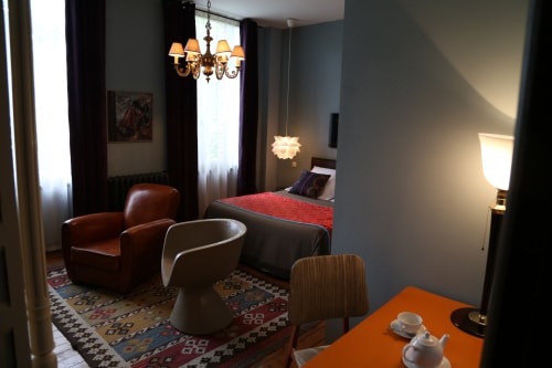 Elegant bedroom at Le Grand Duc in Valenciennes with leather seating, decorative chandelier, and city views
