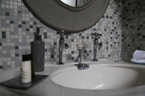 Luxury bathroom sink with chrome faucets, mosaic tile backsplash, and toiletries at Le Grand Duc boutique hotel in