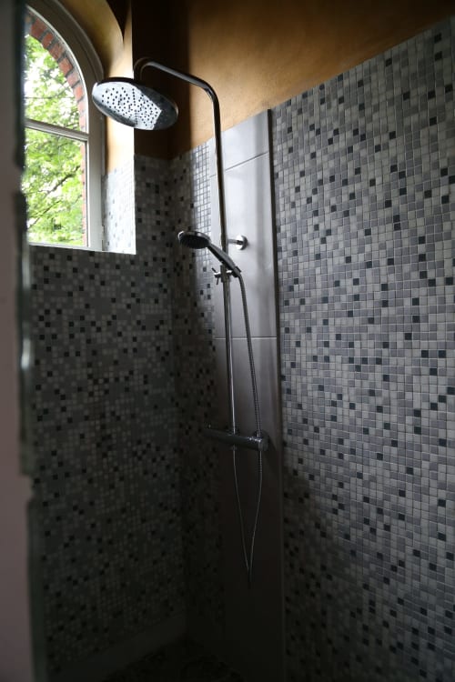 Modern shower in Chapter 1 room at Le Grand Duc, Valenciennes, with mosaic tile walls, rainfall showerhead, and natural