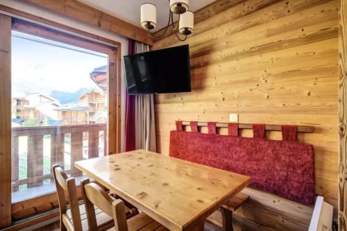 Appartement vue montagne au CMD Méribel avec intérieur bois, table à manger, tête de lit rouge, TV écran plat et balcon aux Allues