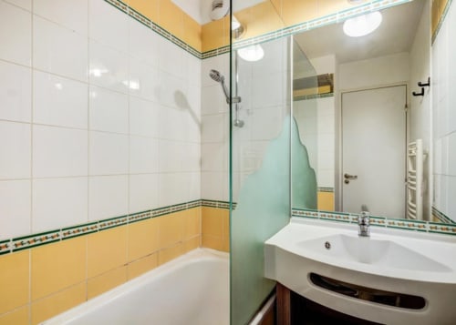Salle de bains moderne aux carreaux jaunes et blancs, douche vitrée, lavabo blanc et sèche-serviettes chauffant au CMD Méribel Le