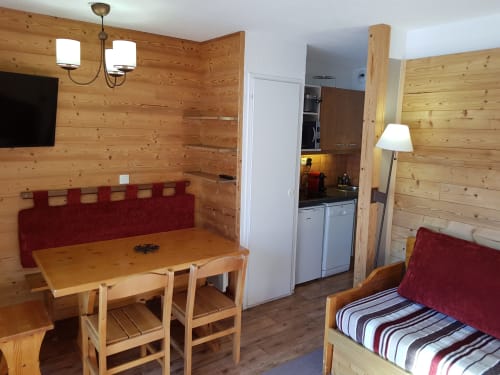Studio cosy en bois au CMD Méribel Le Pralin avec table à manger, cuisine et lit à tête de lit rouge