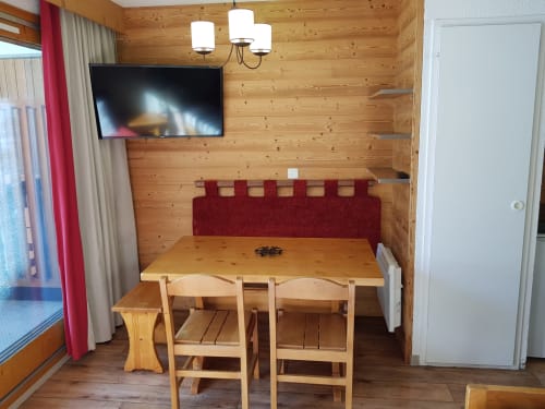 Salle à manger chaleureuse aux boiseries, TV, table en bois, chaises et banquette bordeaux à CMD Méribel Le Pralin