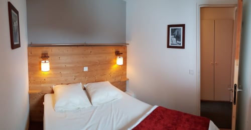 Chambre douillette au CMD Méribel Le Pralin avec tête de lit en bois, literie blanche et éclairage chaleureux à Méribel