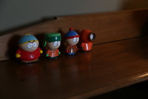 Four South Park character figurines displayed on wooden shelf in Le Grand Duc room, Valenciennes