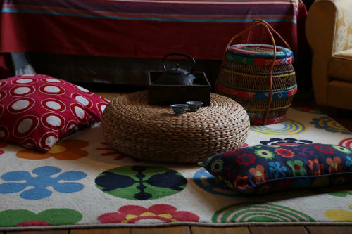 Cozy room detail at Le Grand Duc B&B in Valenciennes with woven basket teapot, colorful pillows, and patterned floor rug.