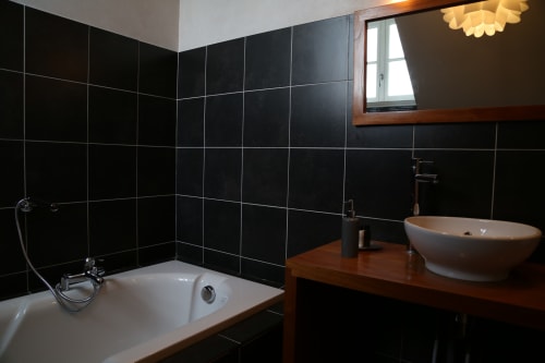 Modern bathroom at Le Grand Duc B&B in Valenciennes with black tiled walls, white bathtub, vessel sink, and wooden vanity