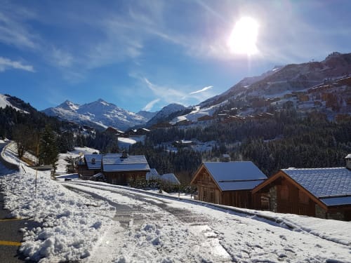 Village alpin enneigé avec chalets en bois, montagnes enneigées, forêt et ciel ensoleillé à CMD Méribel Le Pralin