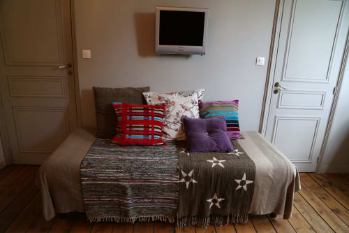 Chambre du Le Grand Duc B&B à Valenciennes avec lit, coussins colorés, TV murale et parquet
